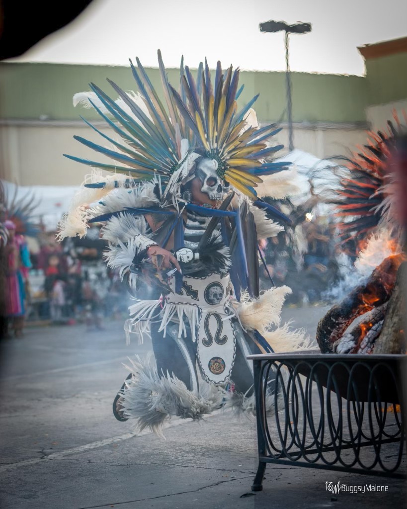 Aztec dancer with skull face paint and feathered headdress performing by fire